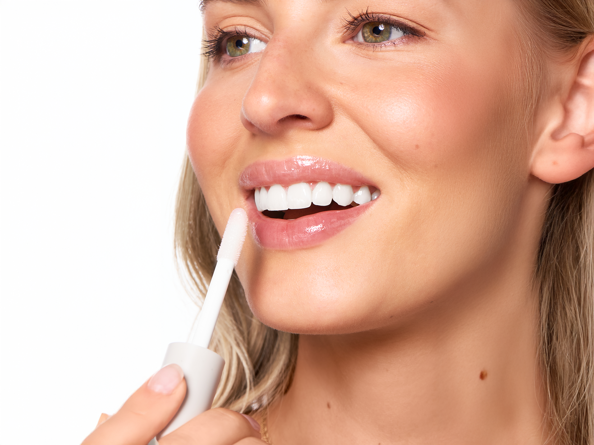 Smiling blonde model with glowing skin applying clear lip oil with a doe-foot wand applicator, close-up of glossy natural lips, soft natural light, clean white background