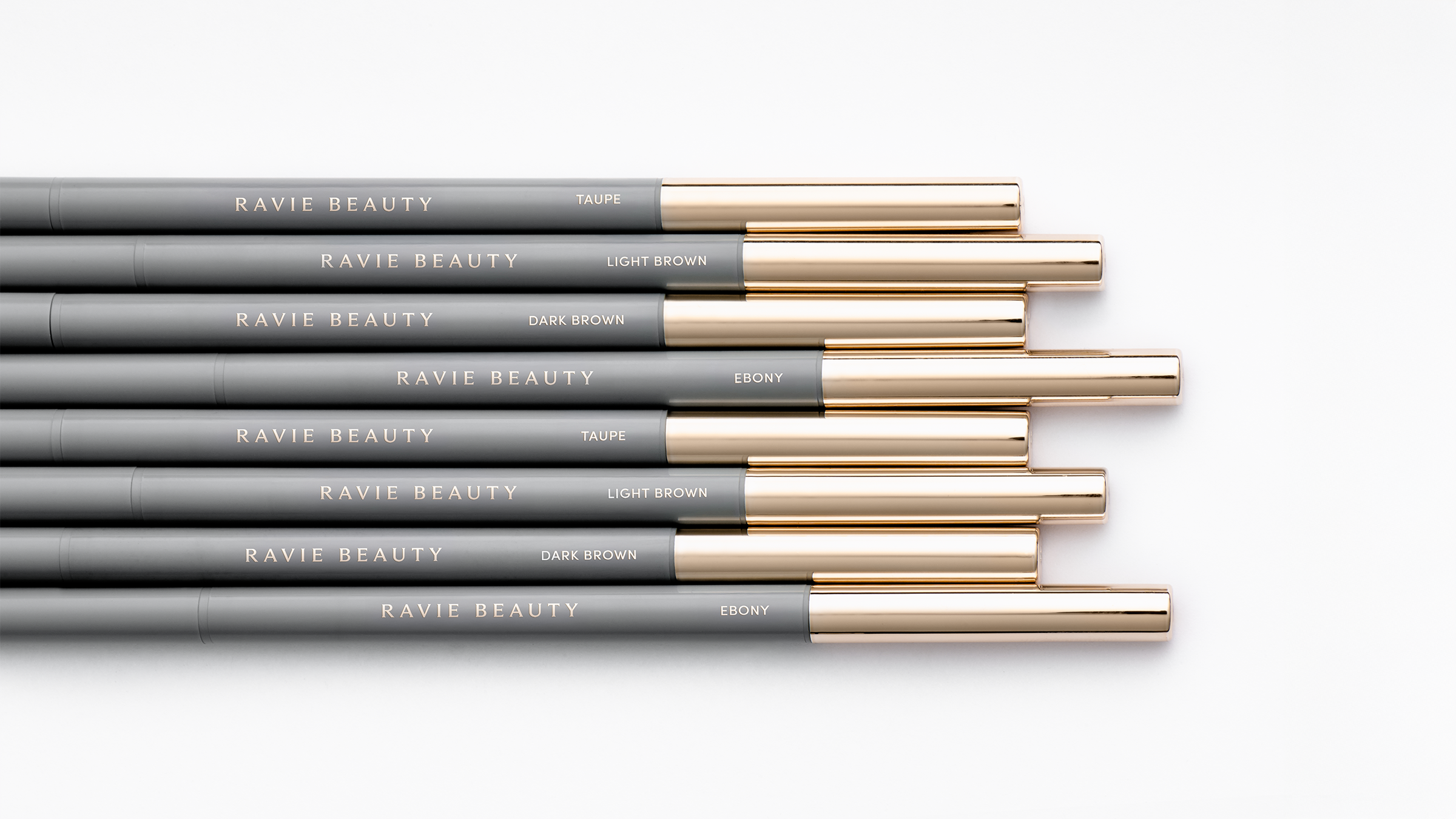 Flatlay of Ravie Beauty Easy Everyday Brow Pencils in Taupe, Light Brown, Dark Brown, and Ebony shades fanned out on a clean white surface, soft natural light