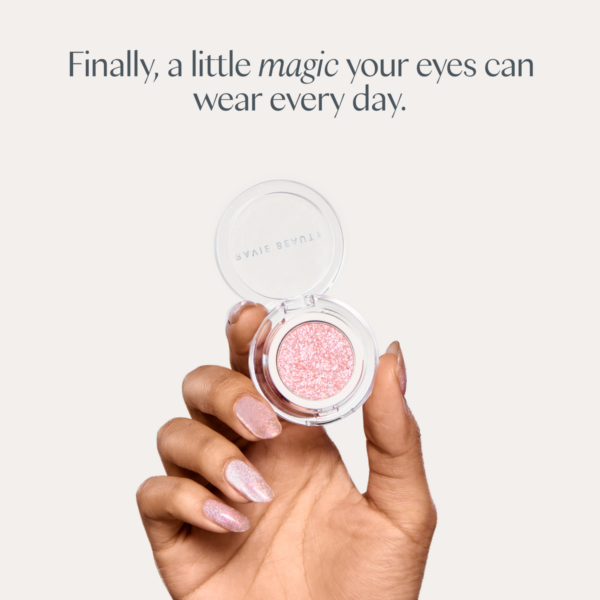 Finally, a little magic your eyes can wear every day. A hand holding the open compact. Ravie Beauty Softlight™ Glistening Eye Topper in Soft Pink