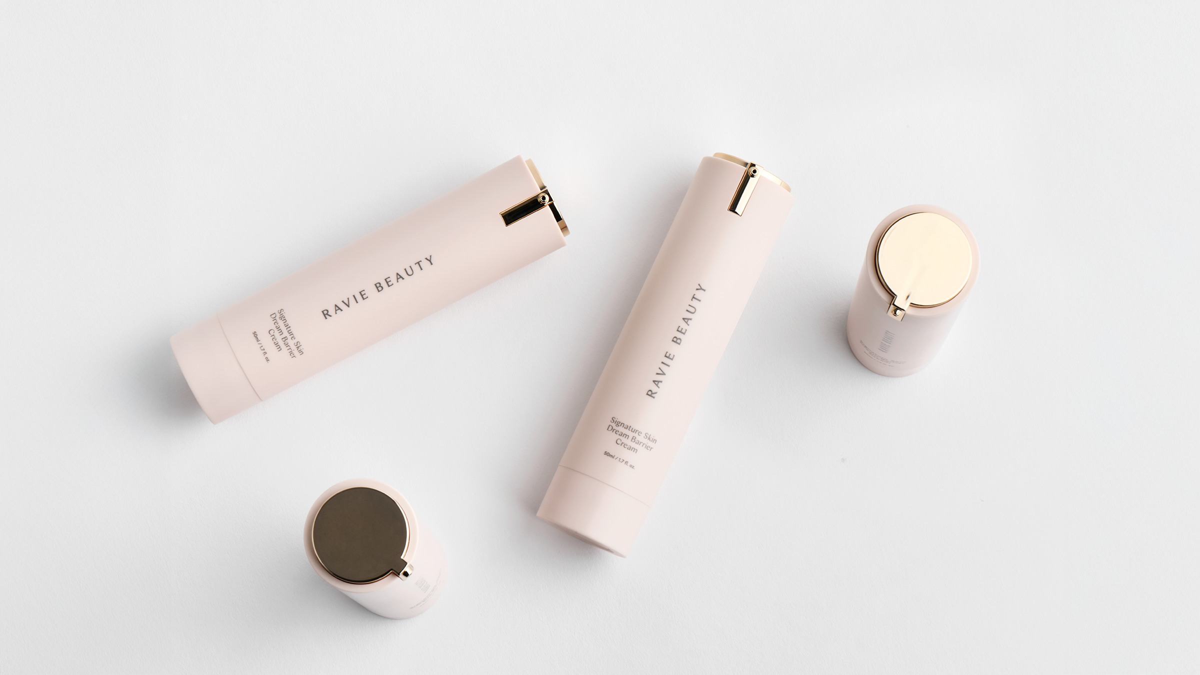 Ravie Beauty product flatlay on a pale grey surface featuring the Signature Skin Dream Barrier Cream airless pump and Effortless Lips bullets with rose gold caps, soft natural light