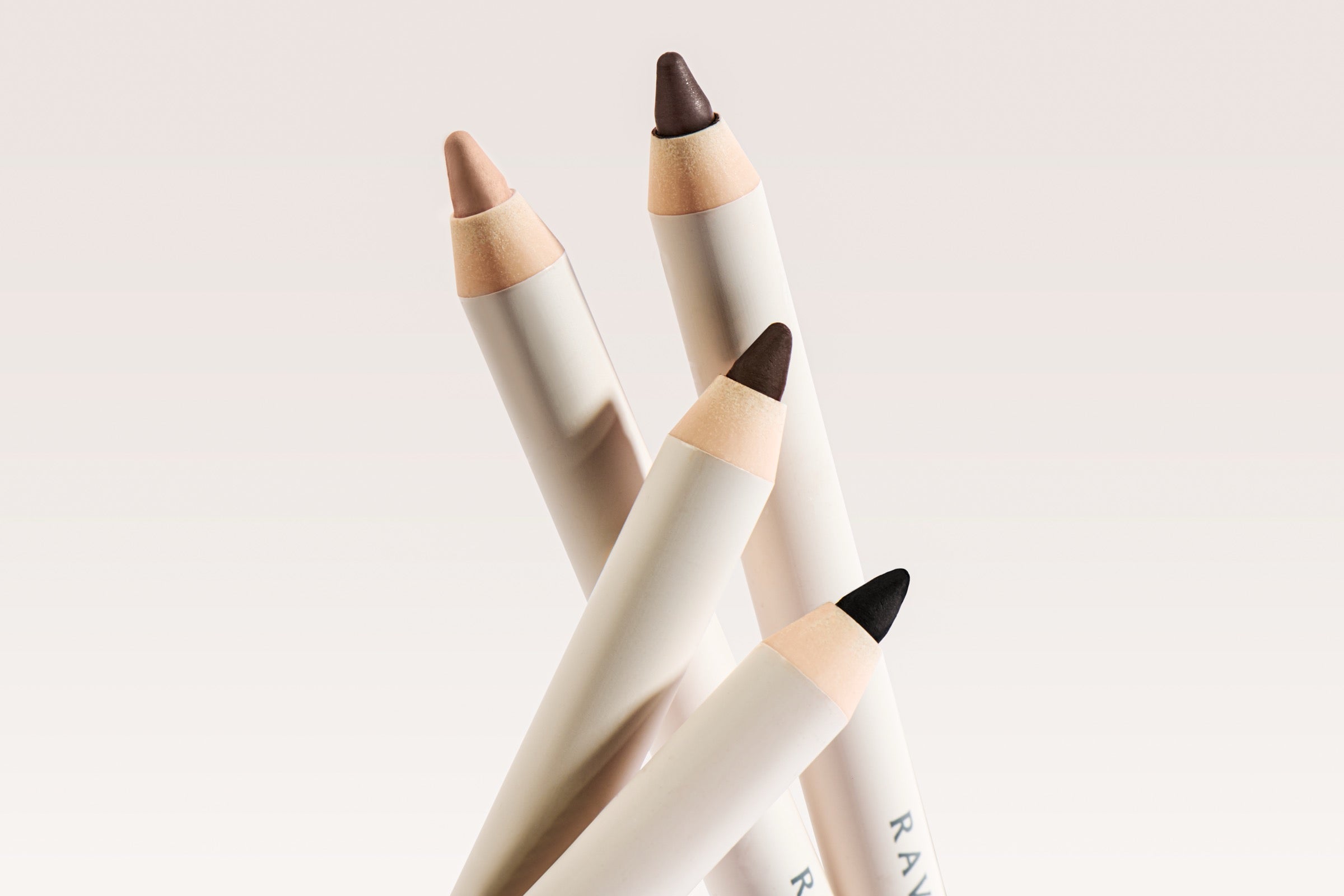 Ravie Beauty Soft Definition Longwear Eyeliner four-shade lineup (Onyx, Umber, Drift, Dune) with the custom angled brush exposed, soft natural light