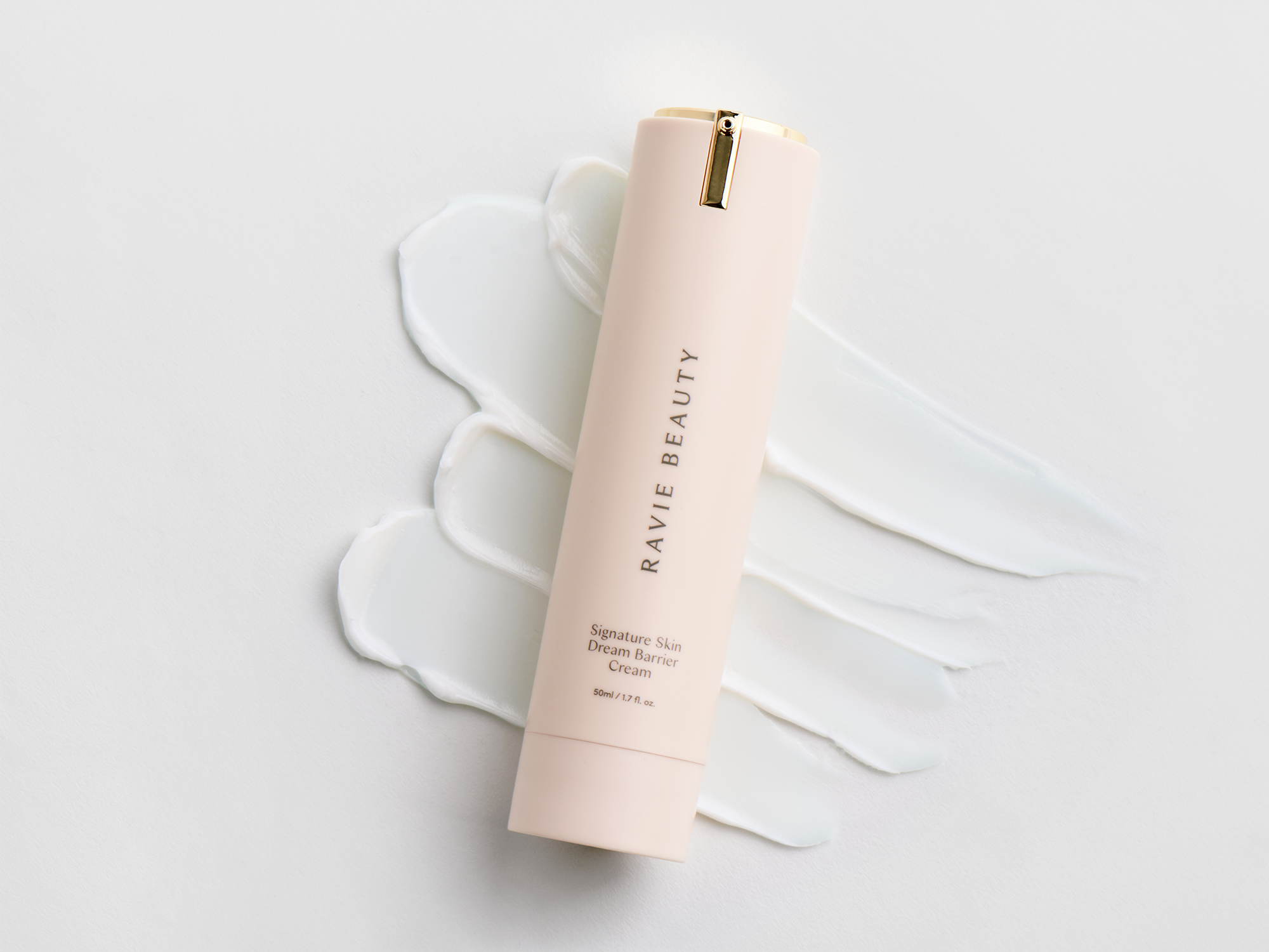 Ravie Beauty Signature Skin Dream Barrier Cream airless pump tube laid against a textured white cream swatch on a clean pale surface, soft studio light, minimal product styling