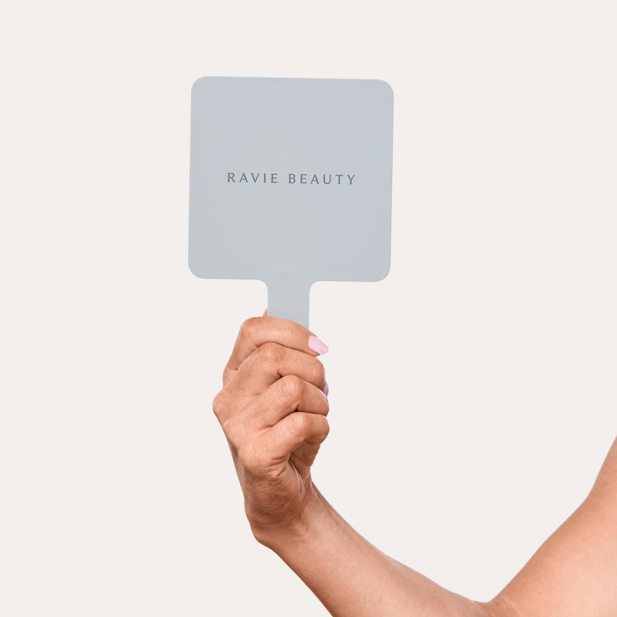 The Hand Mirror held up in one hand, with the Ravie Beauty name on the back. Ravie Beauty The Hand Mirror