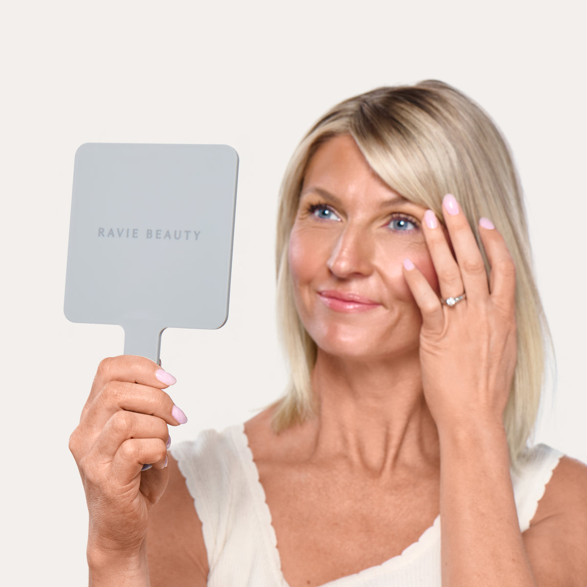 A woman looking into The Hand Mirror for a quick touch-up. Ravie Beauty The Hand Mirror